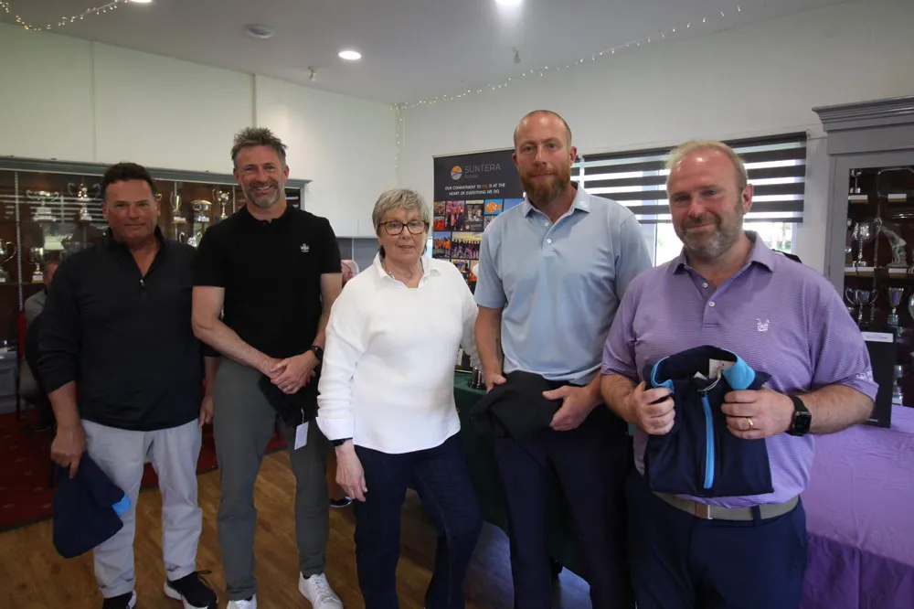 The players from the Suntera team are being presented with their prizes by Janet Henthorn in the clubhouse. All are smiling for the camera.