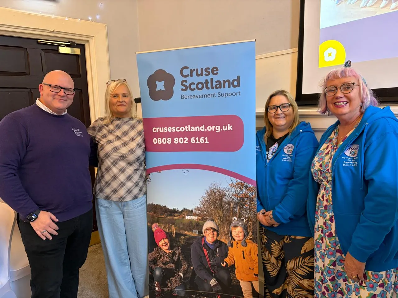 John, Fiona from Cruser Scotland, Claire and Mary are all standing next to a Cruse Scotland banner is the hall of a hotel. All are smiling for the camera.