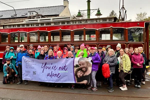 All the walkers on the day (about 40 people) are all stood in hiking clothes in fron of one of th electric trams at Laxey station. A large purple Cruse banner is beinig held out in front of them and everyone is smiling for the camera.