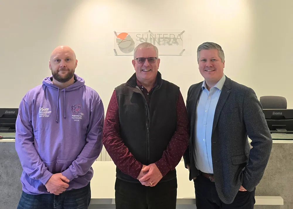 Mark, Sam, and Mark are standing next to each other and smiling for the camera in the reception area of Suntera Global with the Suntera Global logo on the wall behind them.